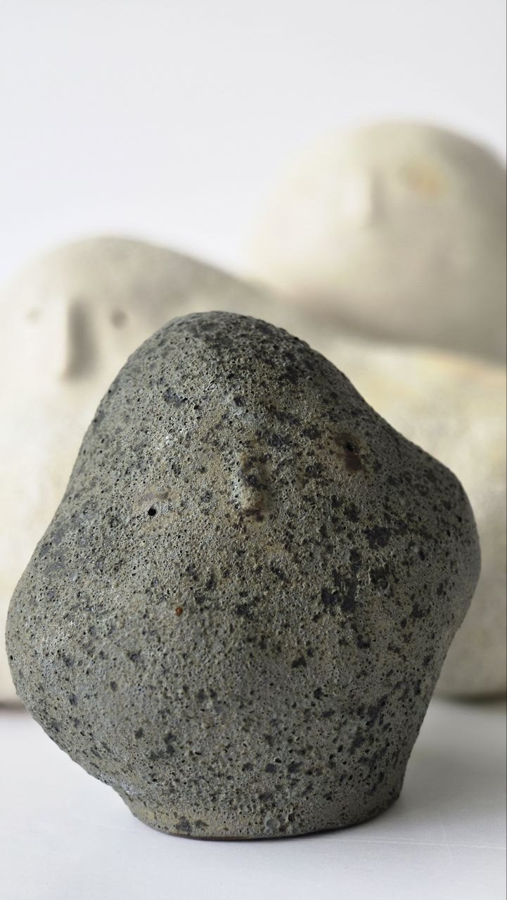 Dark speckled ceramic figure, two pale figures resting behind it