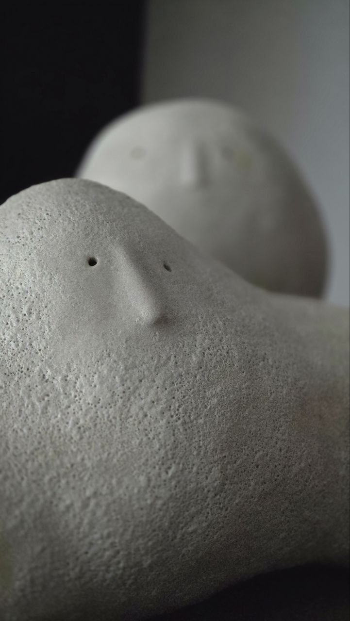 A pale ceramic figure in front, another softly out of focus behind